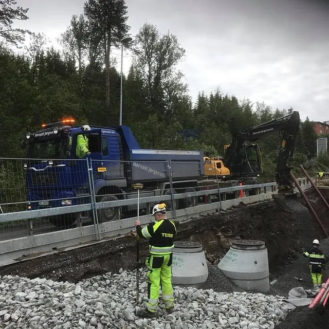 Anleggsarbeidere jobber ved grøft, mens lastebil og gravemaskin fra Norvald Jørgensen står på veien over.