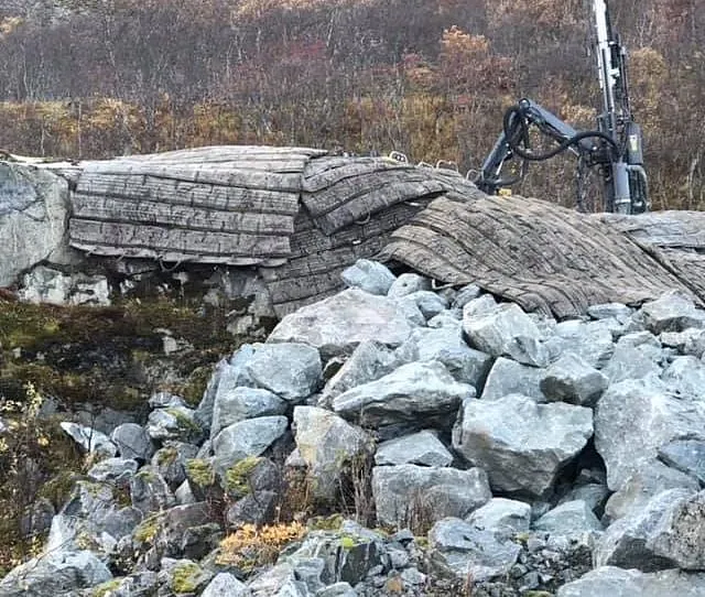Fjellside med store steiner og beskyttelsesmatter, borerigg i bakgrunnen.