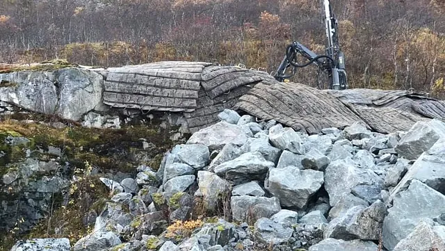 Fjellside med store steiner og beskyttelsesmatter, borerigg i bakgrunnen.