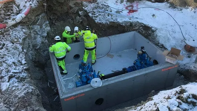 Fire arbeidere i refleksklær jobber i en kum i en snødekt byggegrav.